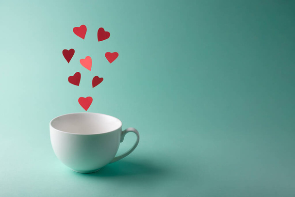 Red hearts flying out of a white cup on a turquoise background, close up, copy space. Valentine's Day card. - Photo, Image