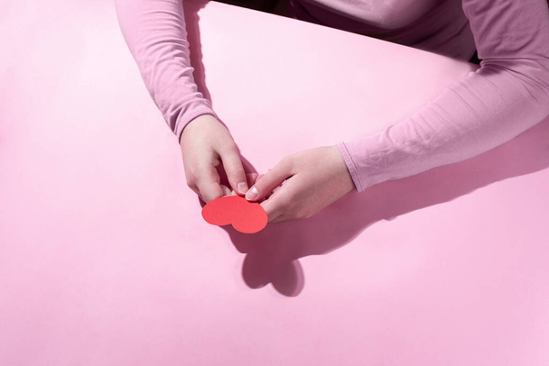 Weibliche Hände halten ein rotes Herz auf rosa Hintergrund im Sonnenlicht, in Großaufnahme. Valentinstag-Karte. Modernes Konzept. - Foto, Bild