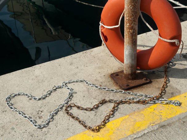 Duas correntes de metal em forma de coração no chão de concreto perto lifebuoy no porto do mar - Foto, Imagem