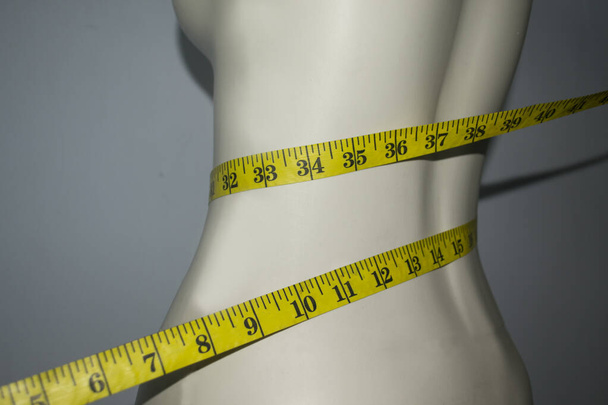 Close up of tape measure on the slim waist of the mannequin. The concept of a weight control diet and slim waist - Photo, Image