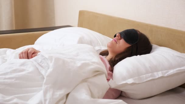 Nuori nainen yllään nukkuva naamio sijaitsee rento modernissa sängyssä - Materiaali, video