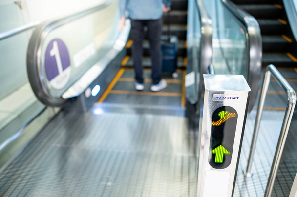 Schody ruchome LED automatyczny znak kierunkowy filar z męskim pasażerem spaceru z walizką w terminalu lotniska. - Zdjęcie, obraz