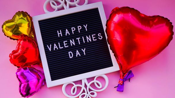 Stylish text frame with the inscription happy Valentine's day on pink backround.Foil hearts balloons red yellow and pink top view of Valentine's Day. Happy Valentine day card or background concept. - 写真・画像