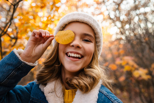Image of young beautiful positive girl walking outdoors in autumn park with leaf in hand - Φωτογραφία, εικόνα