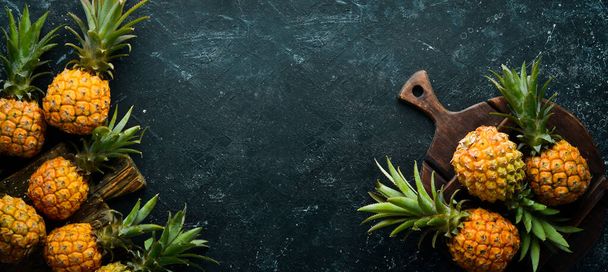 Süße Baby-Ananas auf schwarzem Steinhintergrund. Tropische Früchte. Ansicht von oben. Freiraum für Text. - Foto, Bild