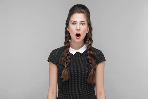 Shocked girl looking at camera with stress and open mouth. Indoor, studio shot isolated on gray background - Foto, Imagen