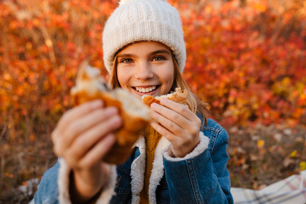 Image of young happy girl outdoors in autumn park drinking tea and eating croissants - 写真・画像