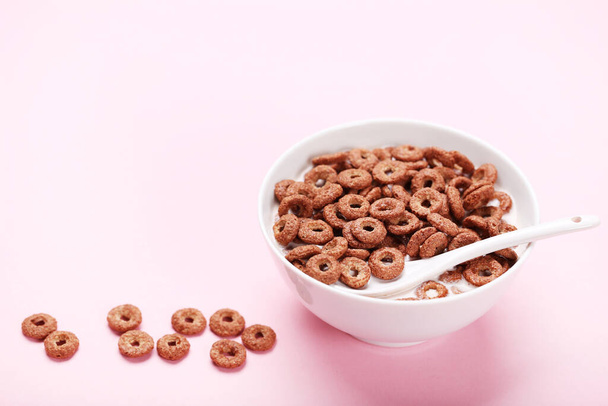 Chocolate corn flakes in bowl with milk and spoon on pink background - Фото, зображення