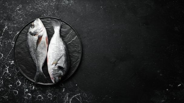 Two dorado fish with spices on a black stone plate. On a dark background. Top view. - Фото, изображение