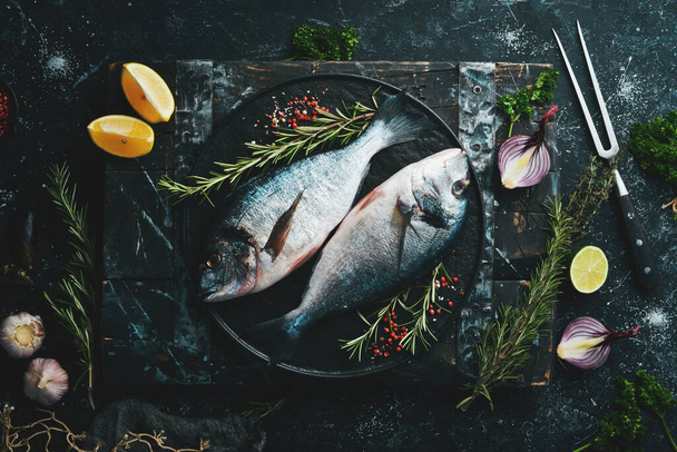 Two dorado fish with spices on a black stone plate. On a dark background. Top view. - Foto, immagini