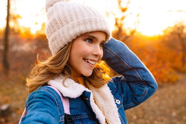 Image of young happy girl outdoors in autumn park taking a selfie by camera - Foto, immagini