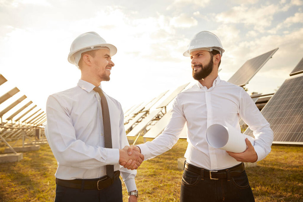 Male partners shaking hands on solar farm - Foto, Bild