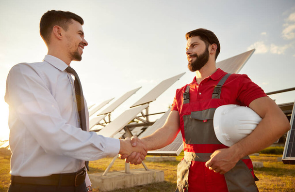 Businessman and engineer shaking hands on solar farm - Foto, imagen