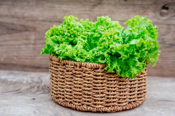 Close up of green leaves of kale in a wicker basket on a wooden background. - Photo, Image