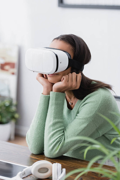 african american designer sitting in vr headset at workplace near headphones, blurred foreground - Foto, Imagem