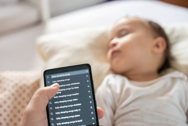 Мама ищет в Интернете, используя свой телефон для ребенка спящие песни - Фото, изображение