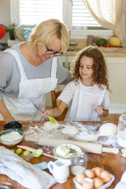 Портрет улыбающейся внучки и бабушки, готовящей вместе. На кухне. Семья на кухне. Вертикальный вид. - Фото, изображение