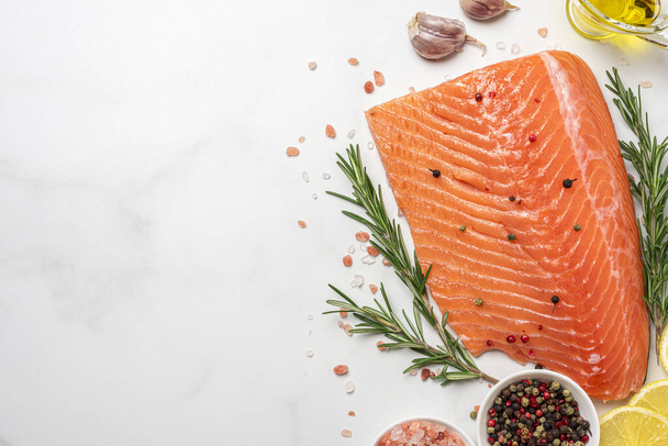 新鮮な鮭の切り身とローズマリーとスパイスが白い大理石の背景にあります。健康的な食事料理。コピースペース付きのトップビュー - 写真・画像