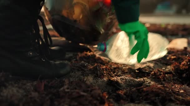 Ein Freiwilliger mit Gummihandschuhen sammelt Müll in einer Plastiktüte ein. Zeitlupe. Nahaufnahme der Füße. Rückansicht. Das Konzept des Umweltschutzes. - Filmmaterial, Video