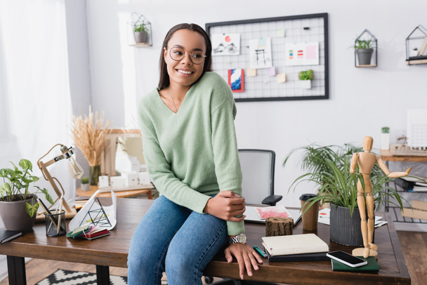 happy african american architect looking away while sitting on work desk at home - Фото, изображение
