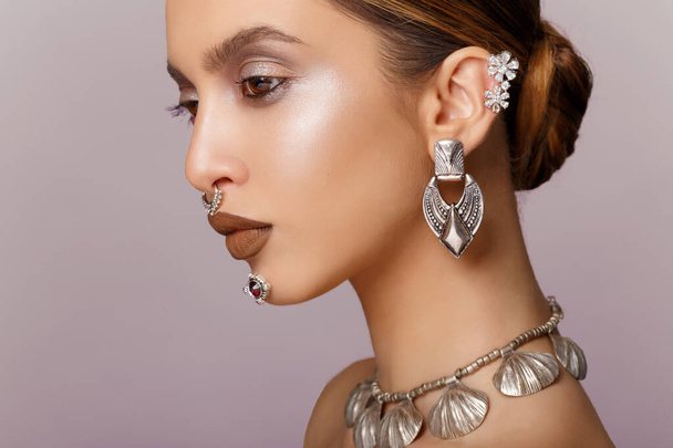 Beauty portrait of young woman with beautiful makeup, looks in profile, earrings and necklace jewelry, arranged hair. - Valokuva, kuva