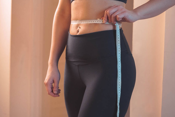 Body Positive. Self Acceptance. Young Woman In Black Sportswear Measuring Waist And Noticing That Is More Than 60 cm. Allow Yourself To Be Happy In Any Fit And Weight - Photo, image