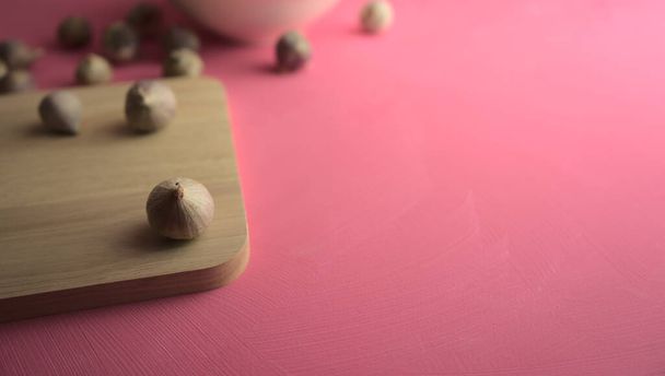アクリル傷ピンクのキャンバスの背景にまな板にニンニク。フード、キッチン、コピースペースで写真を食べる. - 写真・画像
