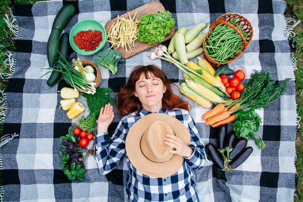 Portret pięknej kobiety rolnik z zamkniętymi oczami i słomkowym kapeluszem leżącym na kratę wśród świeżych warzyw organicznych. Widok z góry. - Zdjęcie, obraz