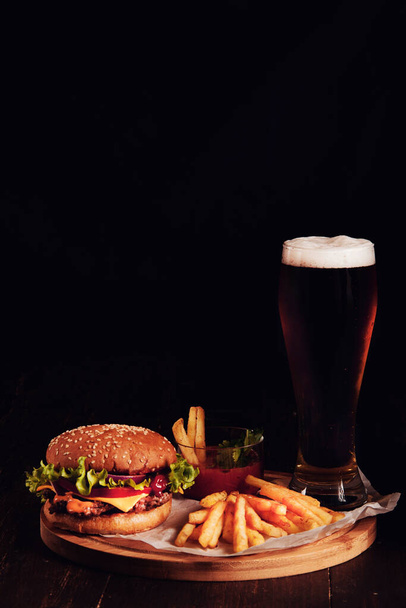 Сендвіч, гамбургер, з картоплею та склянкою пива, на чорному тлі, немає людей, вертикально
, - Фото, зображення