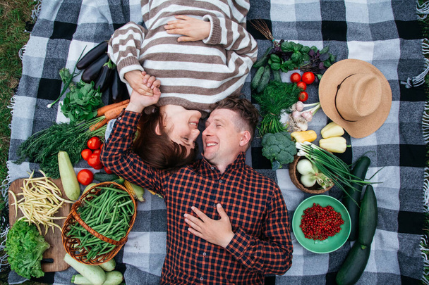 Joyeux couple allongé sur un plaid parmi les légumes biologiques frais. Vue du dessus. - Photo, image