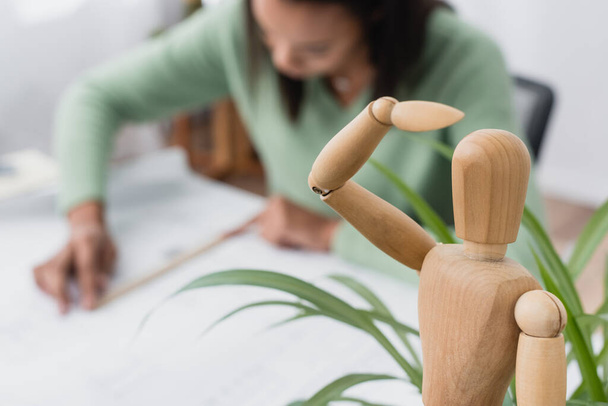 selective focus of wooden human figurine near african american architect working on blurred background - Photo, Image