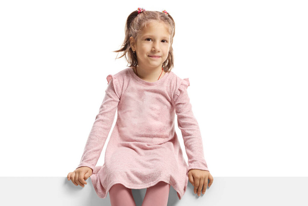 Little girl in pink sitting on a panel and looking at the camera isolated on white background - Photo, Image