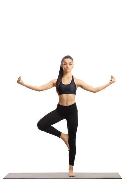 Full length portrait of a young female in a yoga pose on an exercise mat isolated on white background - Photo, Image