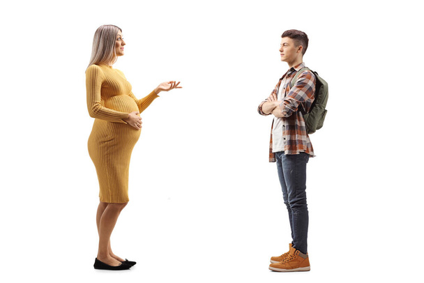 Full length profile shot of a pregnant woman in a yellow dress talking to a teeage male student with a backpack isolated on white background - Φωτογραφία, εικόνα