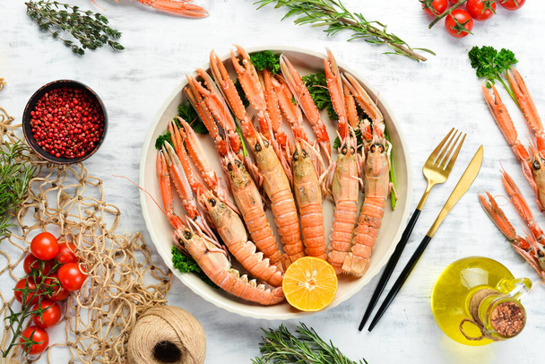 Boiled langoustines with parsley and spices on a plate. Norway lobster on a white wooden background. Top view. Free copy space. - Foto, Bild