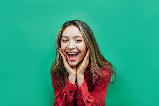Portrait of a pretty girl who sincerely shows the emotion of happiness and surprise looking at the camera on a green background. Place the title of the text. - Fotoğraf, Görsel