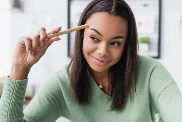 happy african american interior designer touching head with pencil and looking away - Photo, Image