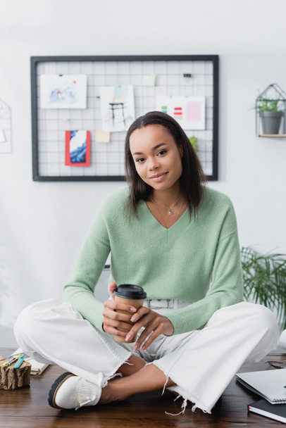 young african american architect sitting on desk with coffee to go and looking at camera - Valokuva, kuva