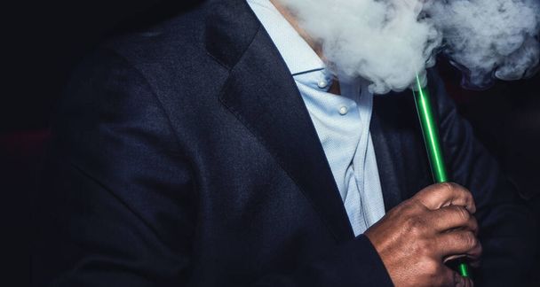 顔のない男がタバコを吸ってるナイトクラブでゆっくりと煙を吐き出してる - 写真・画像