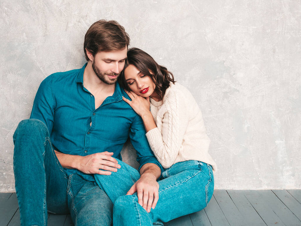 Smiling beautiful woman and her handsome boyfriend. Happy cheerful family sitting in studio on the floor near gray wall.Valentine's Day. Models hugging. Concept of love. Looking at each other - Фото, зображення