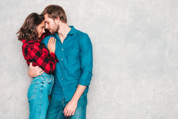 Hot beautiful woman and her handsome boyfriend. Models posing near gray wall in jeans clothes. Young passionate couple hugging before having sex. Sensual pair getting closer for kiss. Lover couple - Фото, изображение