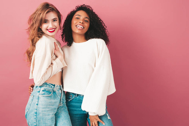 Two young beautiful smiling international hipster female in trendy summer jeans clothes. Sexy carefree women posing near pink wall in studio. Positive models having fun. Concept of friendship  - Φωτογραφία, εικόνα