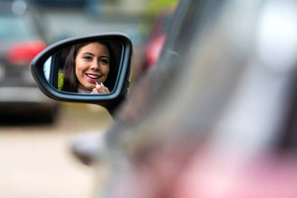 gyönyörű fiatal nő néz hátsó autó tükör alkalmazó rúzs - Fotó, kép