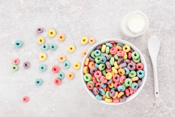 Цветные кукурузные кольца в миске с бутылкой молока на сером фоне - Фото, изображение