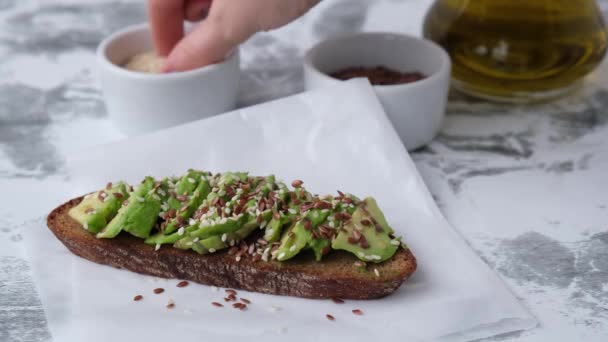 Female hand making Healthy avocado toast on wooden board. Sesame and flax seeds. Vegetarian food. - Footage, Video