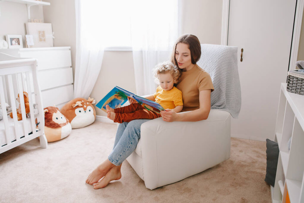 Mom reading book with baby boy toddler at home. Early age children education development. Mother and child kid spending time together. Family authentic candid lifestyle.  - Photo, Image