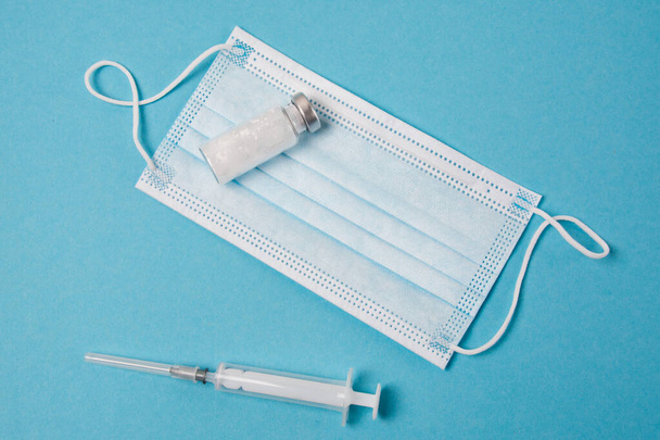 Masque médical, seringue et ampoule avec médicament sur fond bleu. Concept anti-COVID 19. - Photo, image