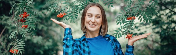 Autumn fall woman portrait. Beautiful happy smiling middle age woman standing in park with red rowan berries on her ear. Silly funny moment. Woman in park outdoor. Web banner header. - Photo, Image