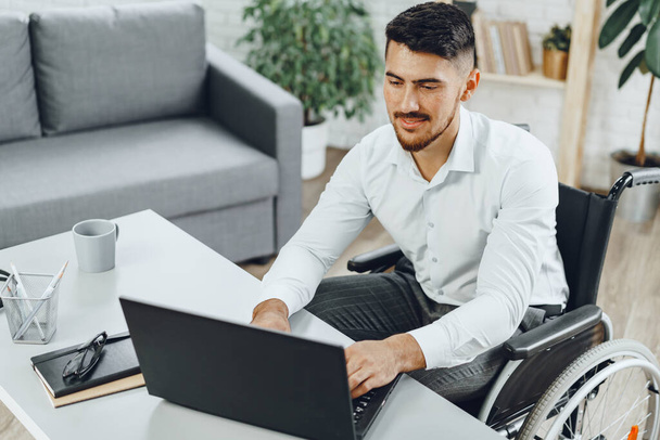 Positive disabled young man in wheelchair working in office - Foto, Bild