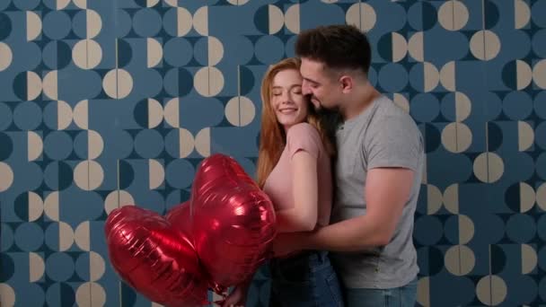 Kaukasischer Mann umarmt seine Ingwerfreundin mit Sommersprossen, nachdem er ihr am Valentinstag rote Luftballons gegeben hat - Filmmaterial, Video